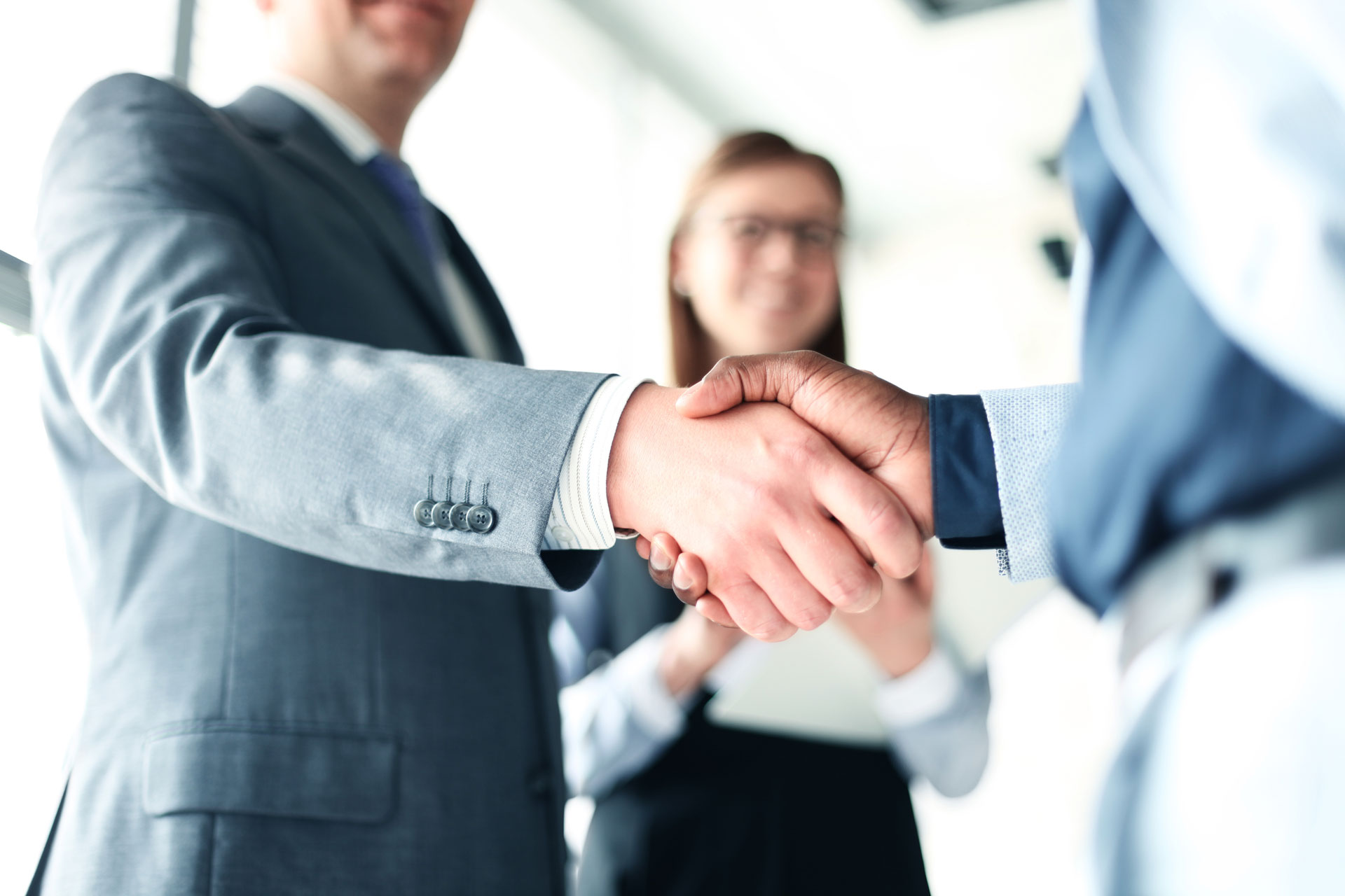 two business people shaking hands in front of a woman.